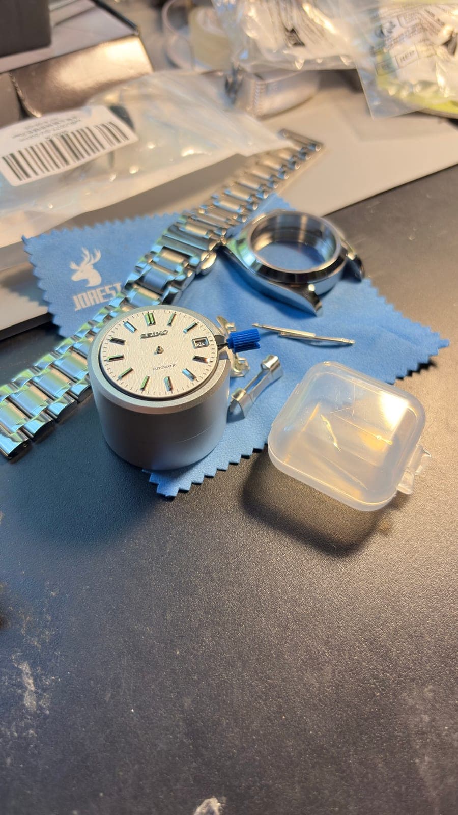 The 002Y's parts on the bench: dial and movement, case, bracelet, hands and crown