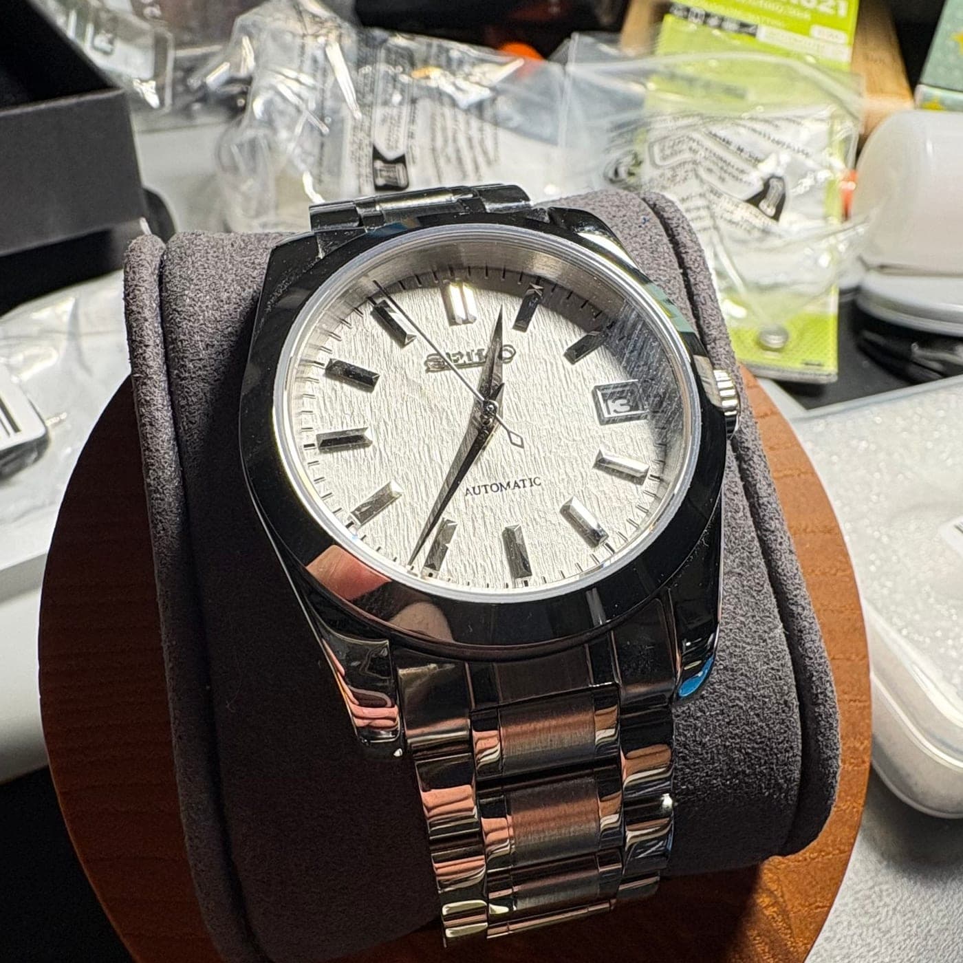 The finished 002Y on a watch stand: textured white dial, polished steel case and bracelet