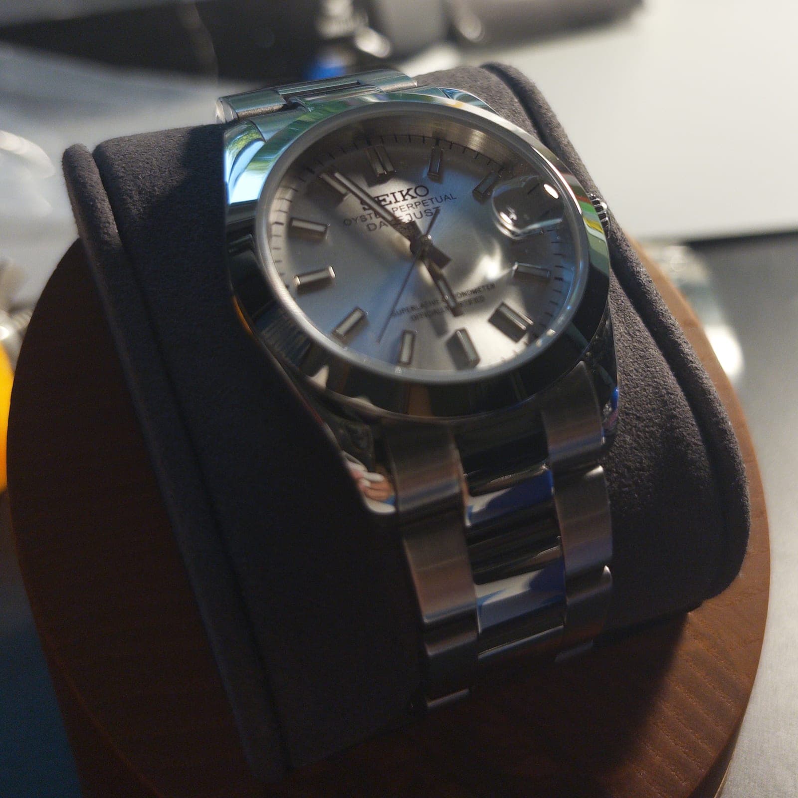The finished watch on a suede cushion at the bench: silver sunburst dial, polished bezel, oyster bracelet